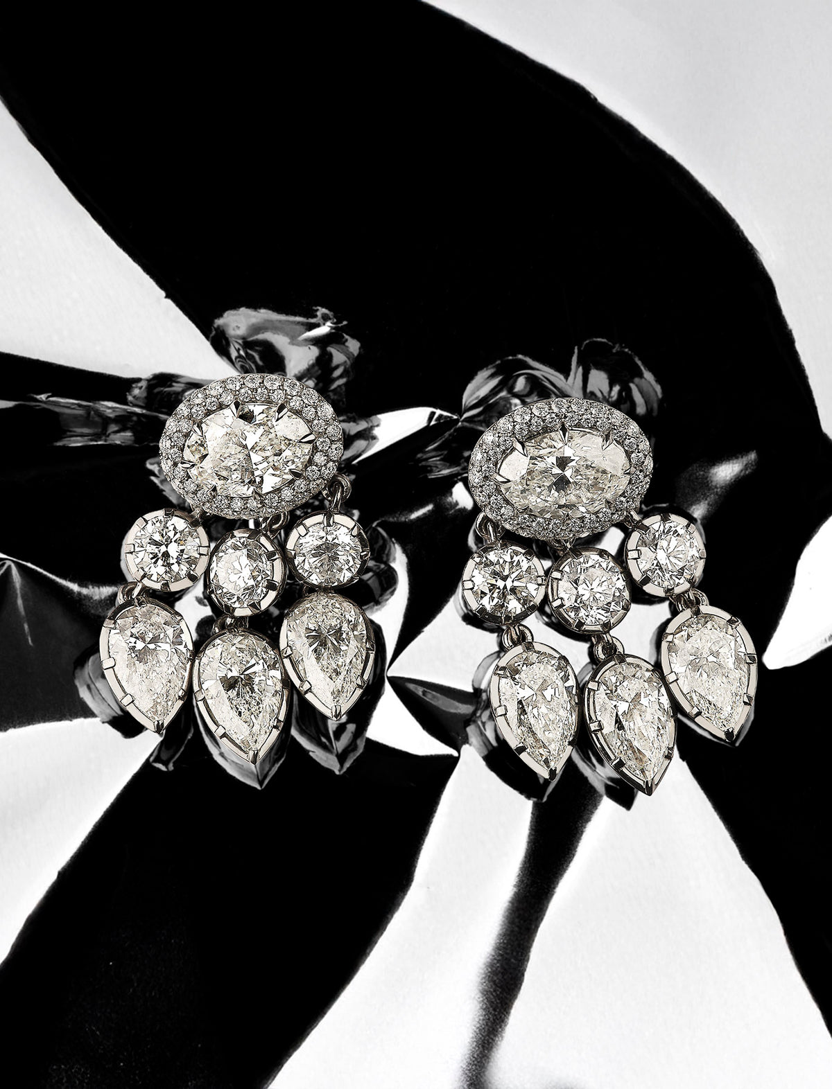 Pair of diamond earrings held by a hand against a black background