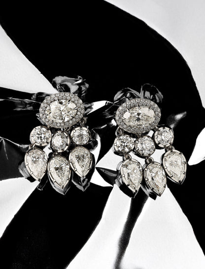 Pair of diamond earrings held by a hand against a black background