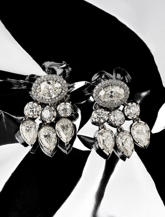Pair of diamond earrings held by a hand against a black background